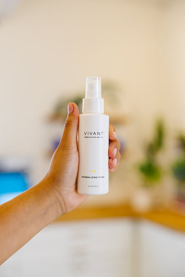 Hand holding a white spray bottle labeled 'Vivant' against a blurred indoor background