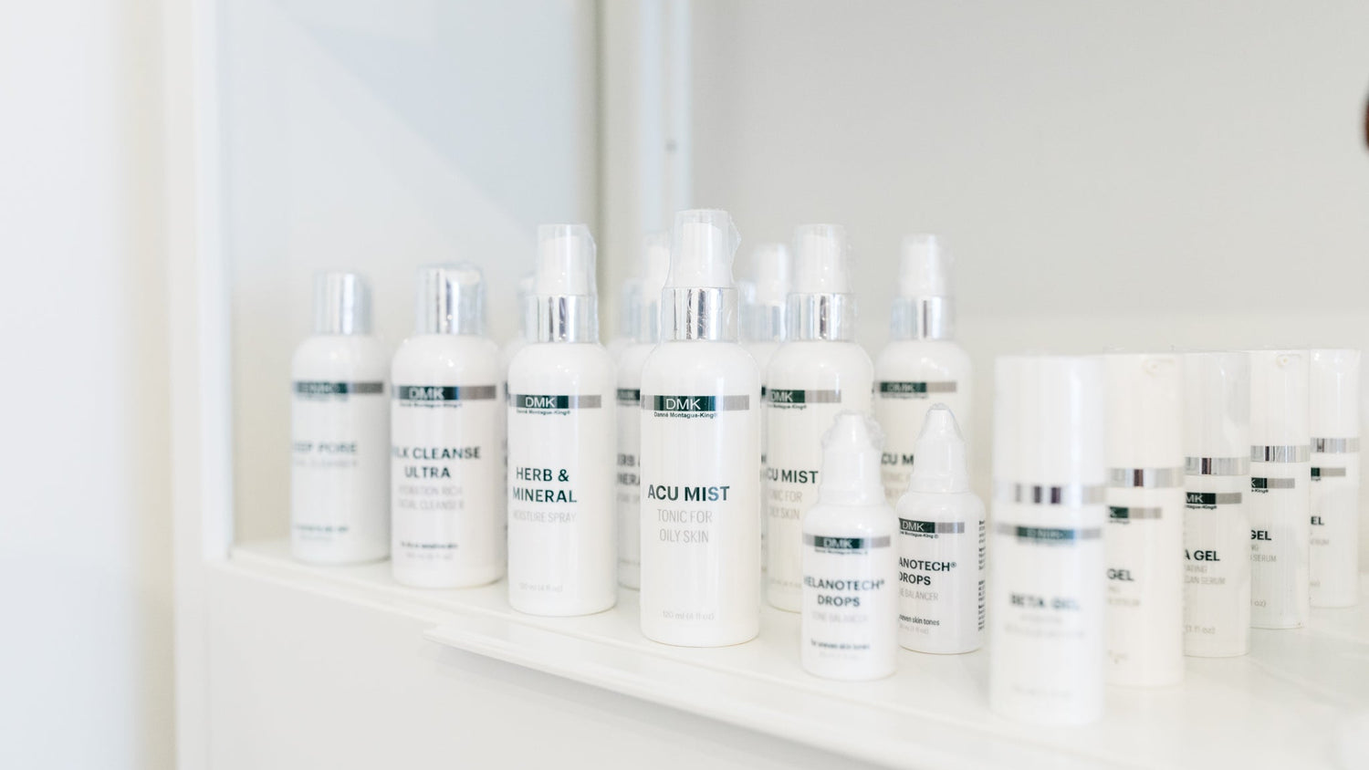 Row of DMK skincare bottles on a white shelf with a blurred background