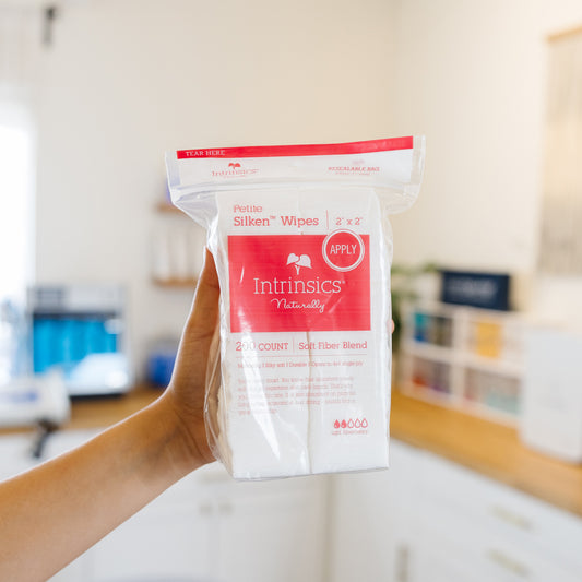 Hand holding a package of Intrinsics Silken Wipes in an estheticians space.