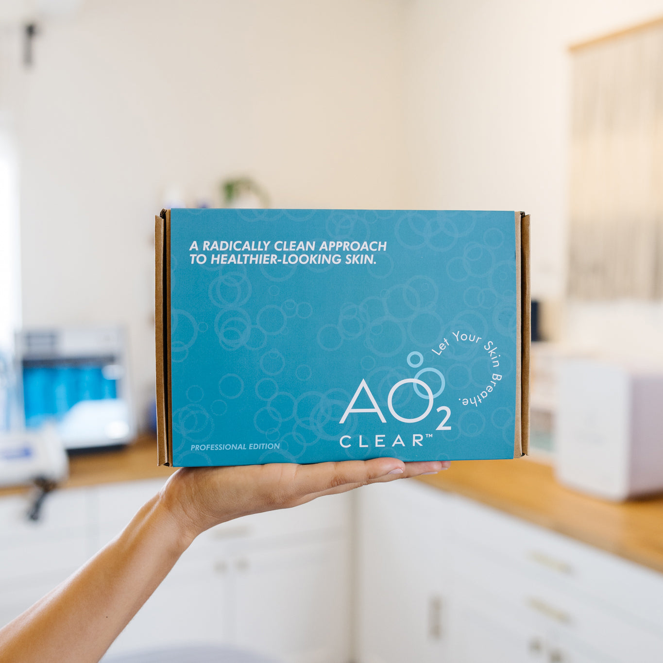 Hand holding a blue AO2 Clear box with text about skincare in an esthetician's office.