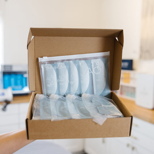 Open cardboard box containing  AO2 clear plastic bags with text, in an esthetician's office.