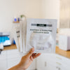 Hand holding DMK soothing and hydrating occlusive mask packets in an esthetician's office.