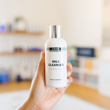 Hand holding a bottle of DMK Milk Cleanser in an esthetician's office.d