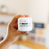 Hand holding a jar of DMK Hydrating Masque in an esthetician's office.