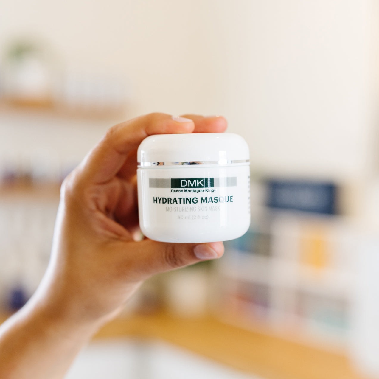 Hand holding a jar of DMK Hydrating Masque in an esthetician's office.