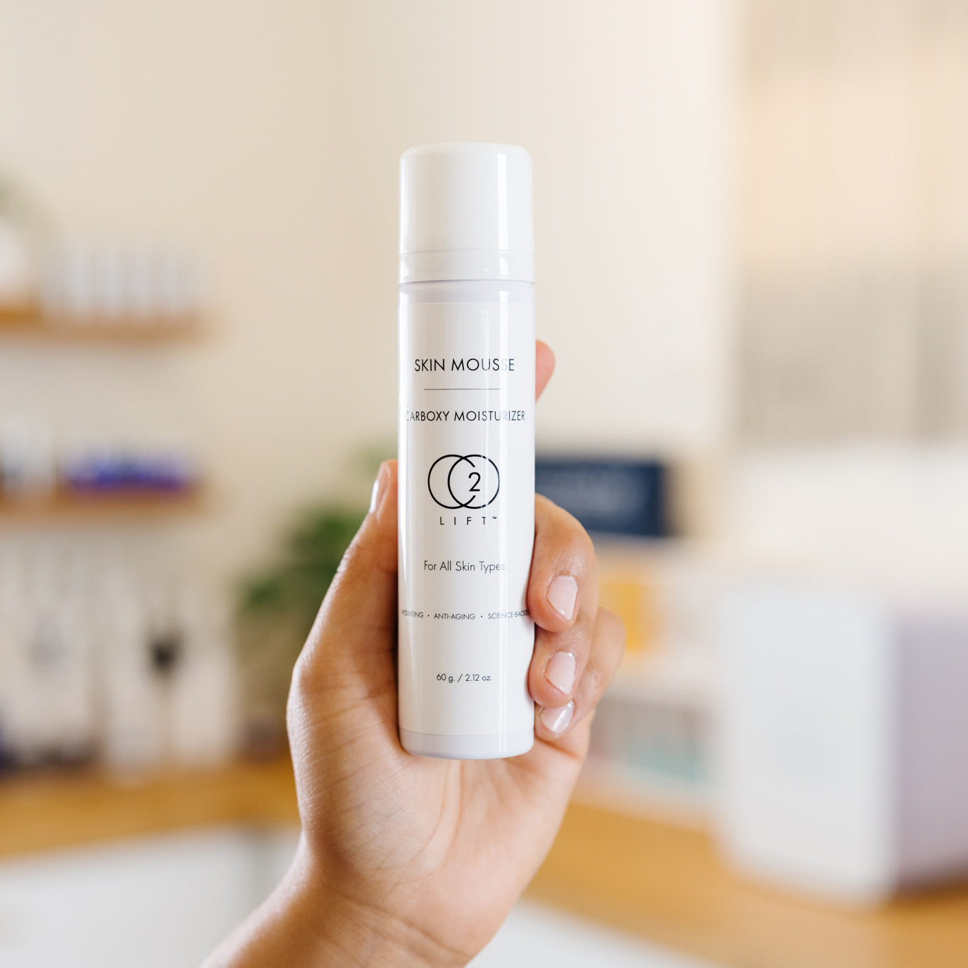 Hand holding a skincare product labeled 'C2 Lift' Skin Mousse in an esthetician's office.