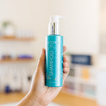 Hand holding a blue FactorFive shampoo bottle labeled 'Shampoo' in an esthetician's office.