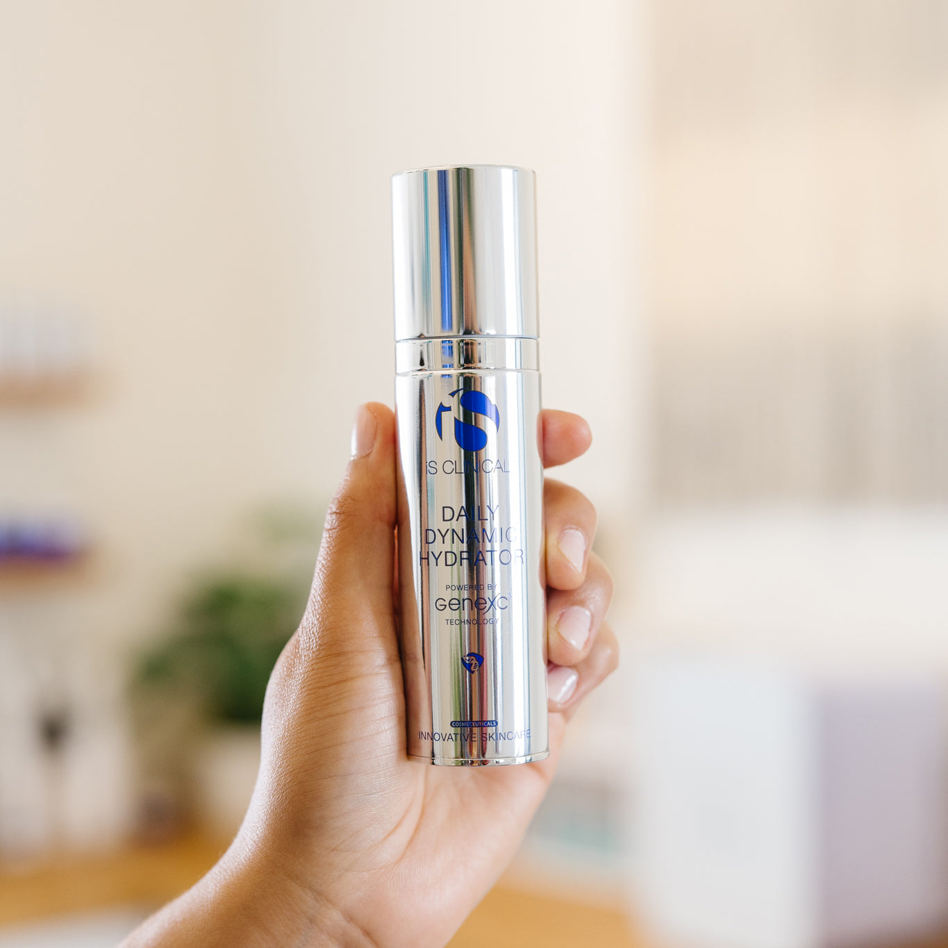 Hand holding a silver iS Clinical Daily Dynamic Hydrator bottle in an esthetician's office.