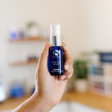 Hand holding a skincare iS Clinical Hydra Cool Serum bottle in an esthetician's office.