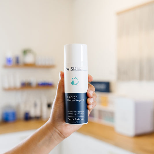 Hand holding a 'Wish' Emerge Biome Repair product  in an esthetician's office.