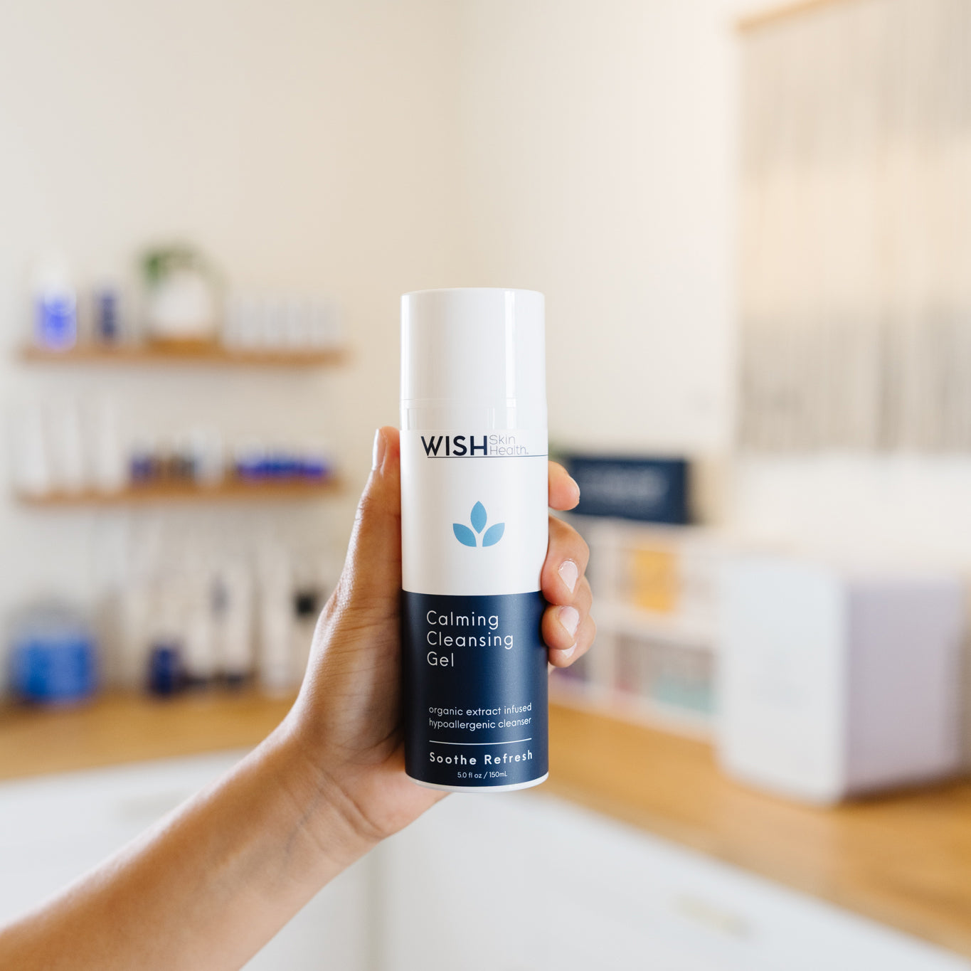 Hand holding a bottle of Wish Calming Cleansing Gel in a kitchen setting