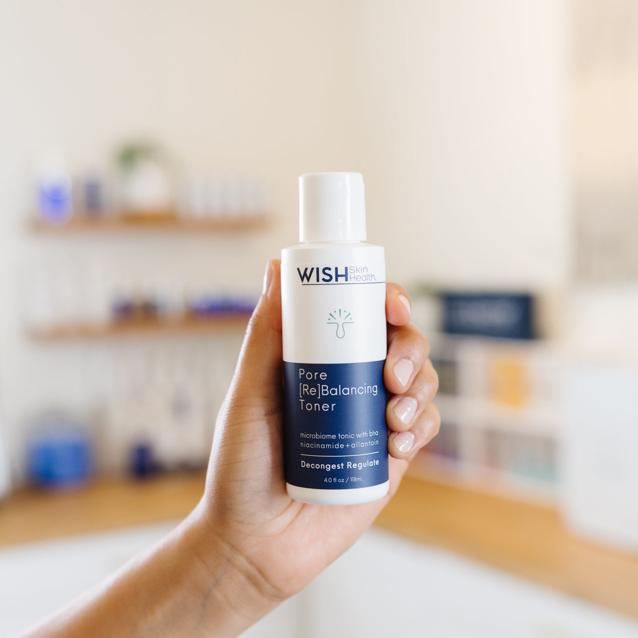 Hand holding a bottle of Wish Pore Balancing Toner in an esthetician's office.