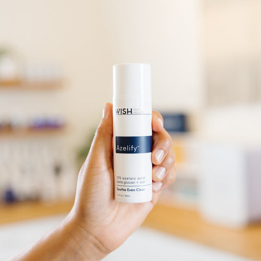 Hand holding a skincare product labeled 'Wish Azelify' in an esthetician's office.