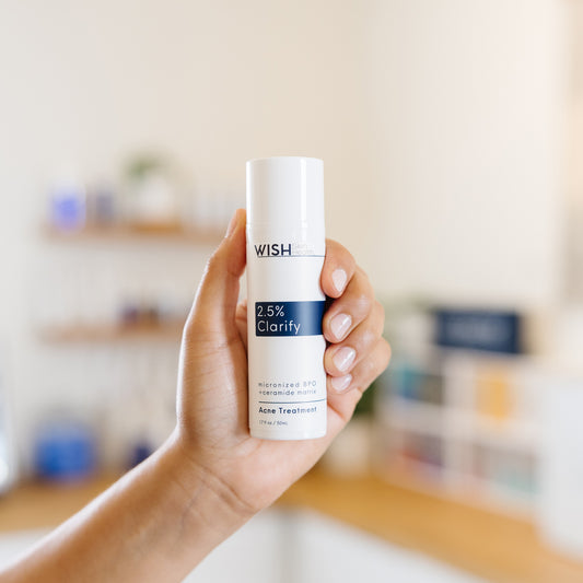 Hand holding a Wish 2.5% Clarify Acne Treatment bottle in an esthetician's office.