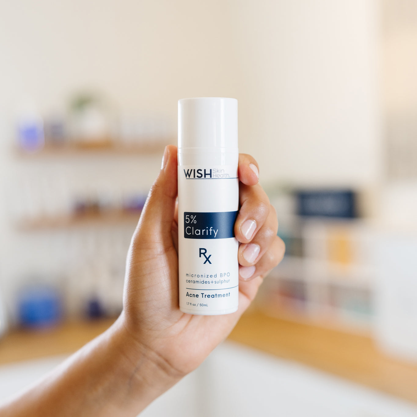 Hand holding a Wish 5% Clarify Acne Treatment bottle in an esthetician's office.