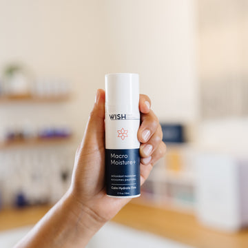 Hand holding a Wish Macro Moisture+ bottle in an esthetician's office.