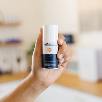 Hand holding a WISH Skin Health C21 Youth Glow Serum in an estheticians office