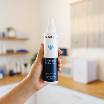 Person holding a bottle of Wish Conditioning Hydra-Mist in an estheticians office