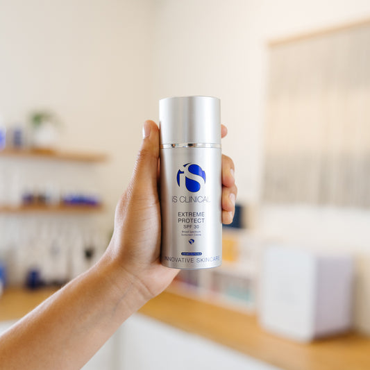 Hand holding a skincare product labeled iS Clinical Extreme Protect SPF 30 in an estheticians office
