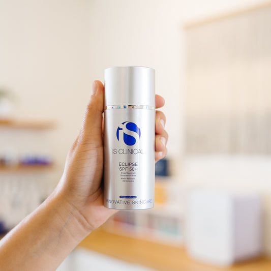 Hand holding a bottle of IS Clinical Eclipse SPF 50 sunscreen in an estheticians office