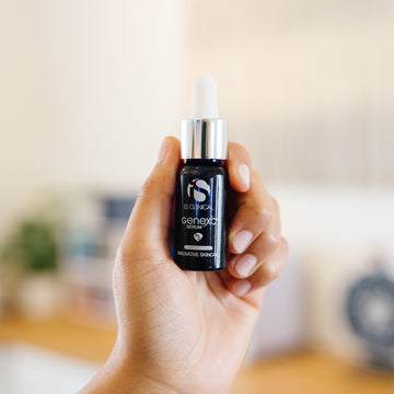 Hand holding a bottle of iS Clinical GenexC Serum in an estheticians office