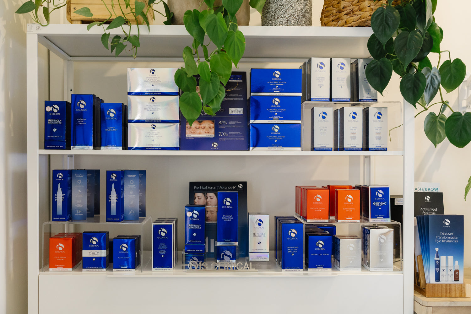 Shelf displaying various boxes and products of iS Clinical Skincare with a plant in the background