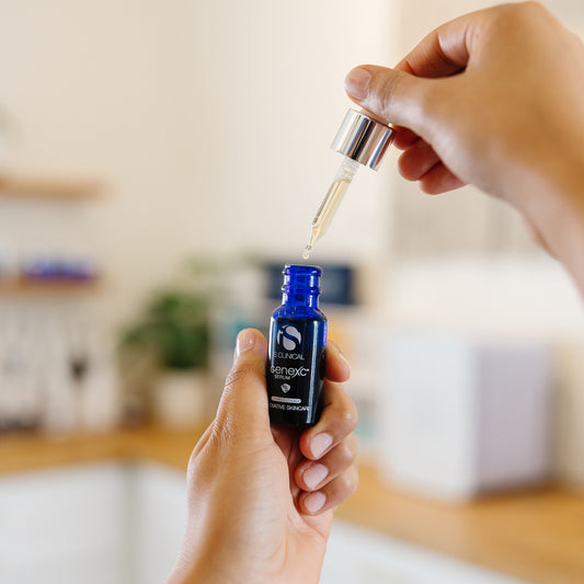 Person holding a bottle of iS Clinical GenexC Serum in an estheticians office