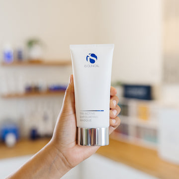 Hand holding a tube of IS Clinical Tri-Active Exfoliating Masque product in an estheticians office