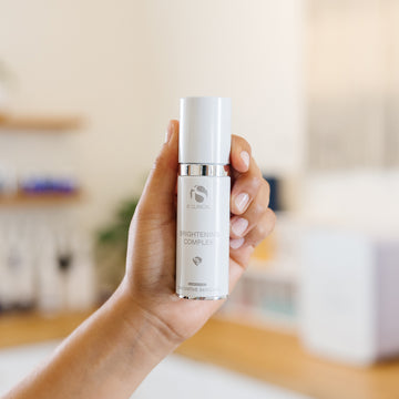 Hand holding iS Clinical 'Brightening Complex' bottle in an estheticians office
