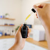 Hand holding a black bottle labeled Vivant Exfol-A with a dropper in an estheticians office