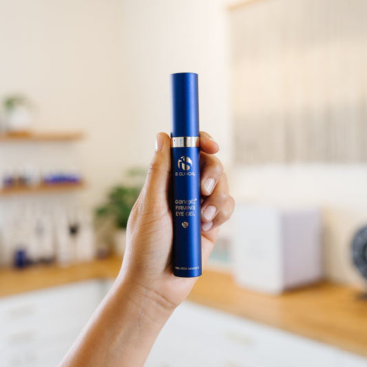 Hand holding a blue iS Clinical Genexc Firming Eye Gel bottle in an estheticians office