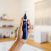 Hand holding a blue iS Clinical Genexc Firming Eye Gel bottle with the lid off in an estheticians office