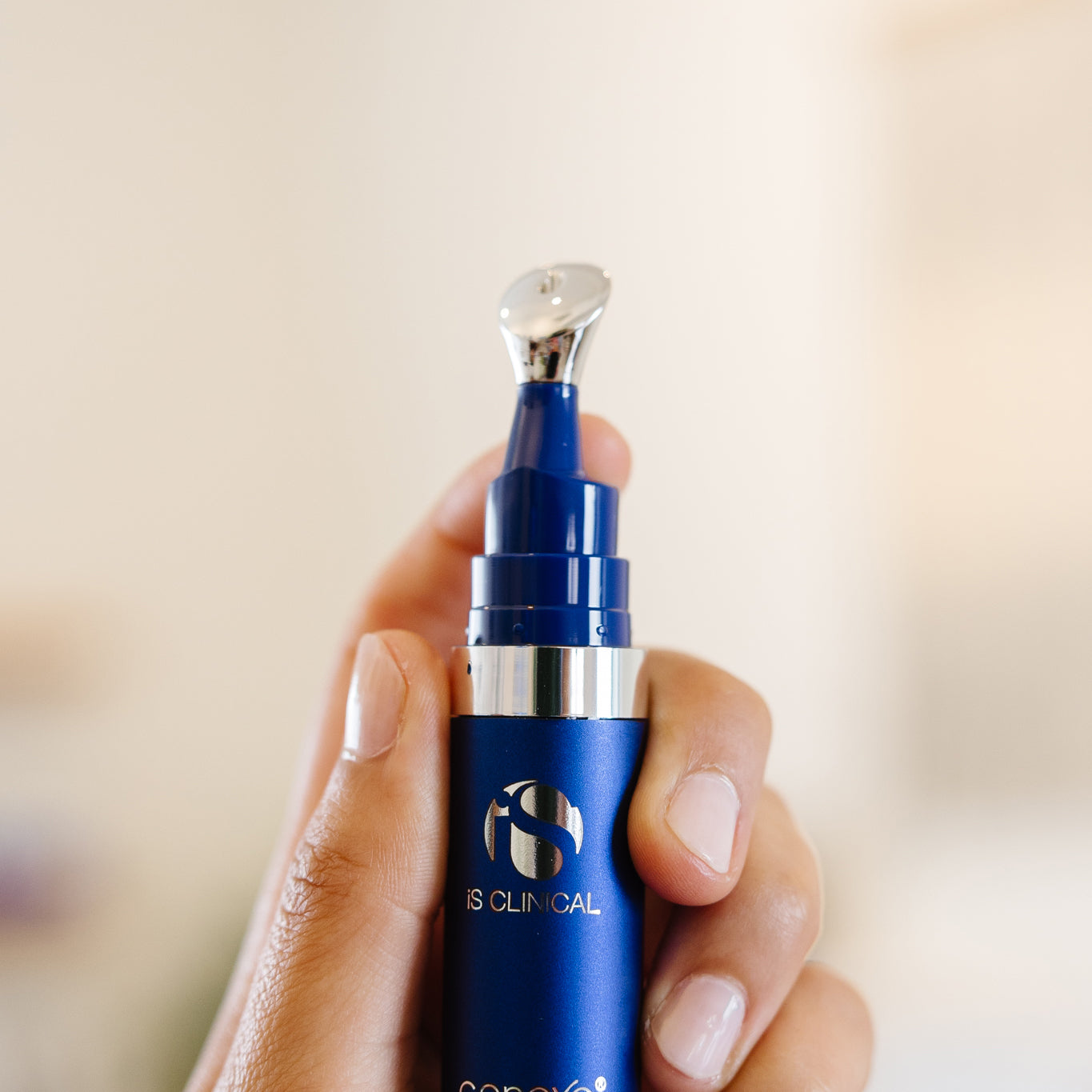 Hand holding a blue iS Clinical Genexc Firming Eye Gel bottle in an estheticians office