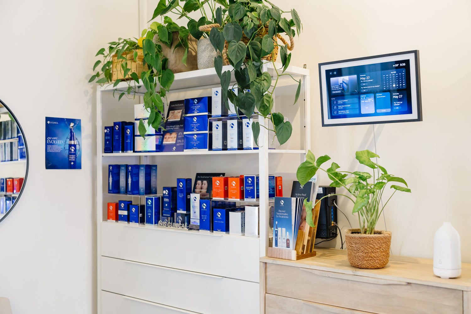 Display of skincare products on shelves with a digital screen and plants in a room setting.