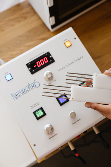 Neurotis device with electronic components and a hand holding a tool on a wood counter in estheticians office