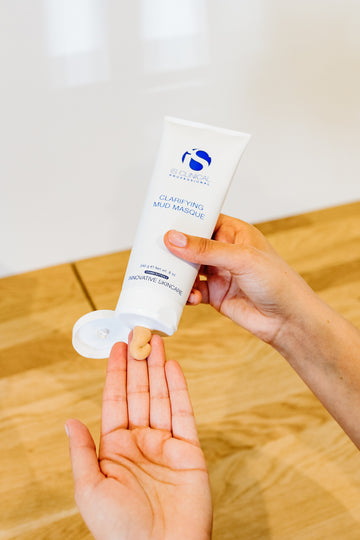 Person holding an iS Clinical skincare product with a wooden surface in the background