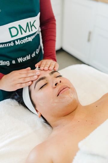 Person receiving a facial treatment with a DMK branded apron in the background