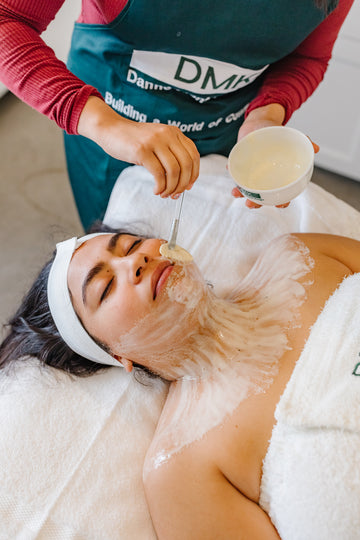Woman receiving a DMK Enzyme Therapy mask with brush on her face